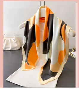 Detail of geometric pattern satin silk scarf with orange and black blocks on a hanger