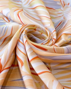 Détail d'un foulard en soie à imprimé feuilles tropicales aux tons orange et bleu