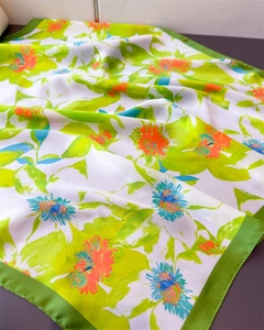 Detailed close-up of vibrant floral print silk scarf with refined green hem stitching