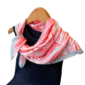 Foulard en soie à motif plume rose et orange sur un cintre en bois avec un gilet noir