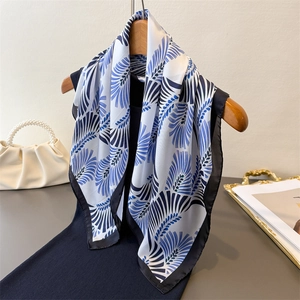 Dettaglio di un foulard in seta con motivo a piume blu e bianche su una gruccia