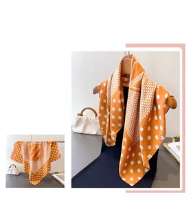 Detailed close-up of orange silk square scarf with classic white polka dots and geometric patterns