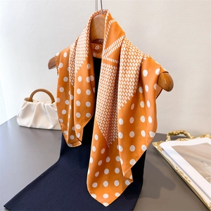 Close-up of elegant orange silk-like scarf with polka dots hanging on a wooden hanger