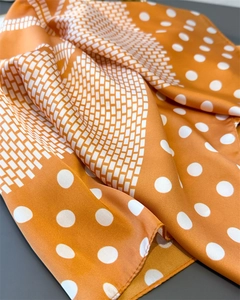 Close-up of orange silk scarf with white polka dots and geometric brick patterns