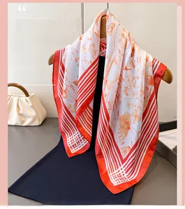 Detail of square silk scarf with orange floral prints and red striped borders on hanger