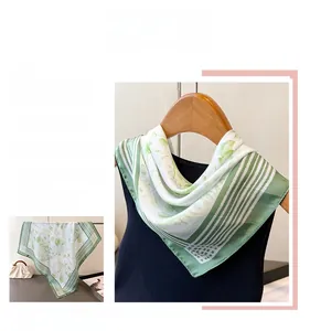 Detailed pattern of a green and white floral silk scarf displayed on a wooden hanger