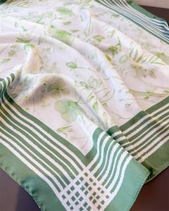 Detailed view of silk-like scarf with green floral patterns and striped edges