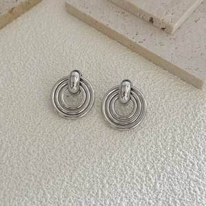 Silver geometric layered disc hoop earrings for women on a textured beige surface