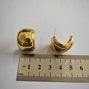 Detailed view of chunky C-shaped gold-plated metal hoop earrings with measurement scale
