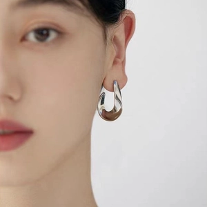 Detail of minimalist irregular silver-tone U-shape hoop earring worn on a model's ear