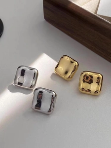 Boucles d'oreilles carrées polies en finitions or et argent sur une boîte en bois
