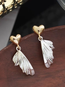 Macro shot of two-tone heart and wing earrings with elegant metal pleat textures