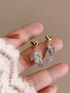 Detail of two-tone heart and wing earrings held to show scale and metallic luster