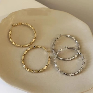 Textured woven hoop earrings in gold and silver finish on a ceramic plate