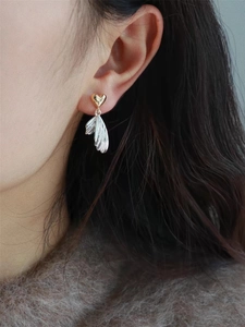 Close-up of gold heart and silver fishtail earrings worn, showing dual-tone metal texture