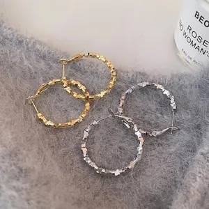 Textured gold and silver hoop earrings with geometric pattern on soft grey knitwear