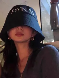 Close-up of black canvas bucket hat with white logo lettering and gold earrings