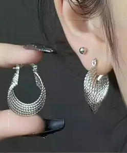 Détail des boucles d'oreilles créoles argentées avec texture tissée sur l'anneau en C