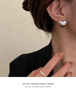 Close-up of 3D heart-shaped silver stud earrings worn by a model in a minimalist style