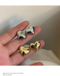 Detailed view of 3D heart stud earrings in polished gold and silver finishes held by hand