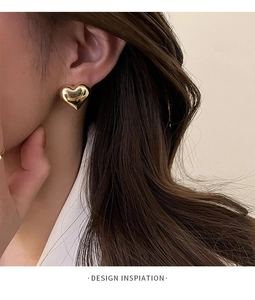 Close-up of a model wearing a shiny 3D heart stud earring in polished gold finish