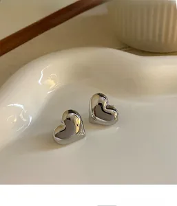 Macro detail of polished 3D heart-shaped silver earrings on white ceramic dish