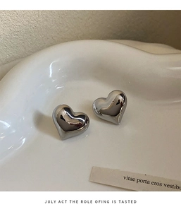 Close-up of silver 3D heart earrings with polished finish on a ceramic tray