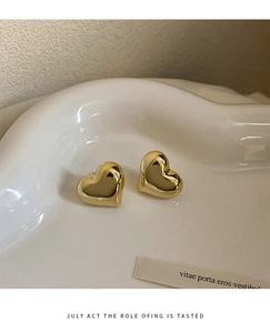 Close-up of polished 3D heart-shaped gold stud earrings on a white artistic ceramic plate