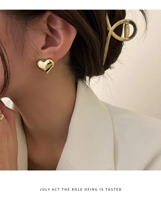 Close-up of polished golden heart-shaped stud earrings worn by a model in a minimalist style