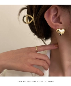 Close-up of golden 3D heart stud earring on model with polished metallic mirror finish