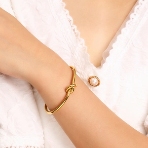 Minimalist gold knot cuff bracelet on wrist, adjustable open design for women