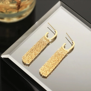Detailed view of long gold tassel drop earrings with C-shape studs on a reflective surface