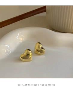 Macro shot of 3D polished gold heart stud earrings on a white ceramic jewelry tray