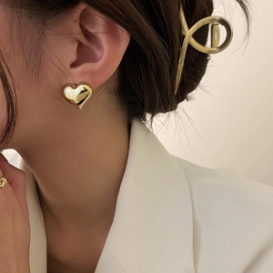Elegant gold 3D heart stud earrings with mirror finish worn by a model in white blazer