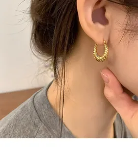 Close-up of a woman wearing these golden twisted croissant hoop earrings in a lifestyle shot