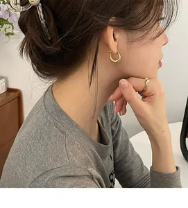 Detail of model wearing gold twisted hoop earrings and a minimalist smooth band ring