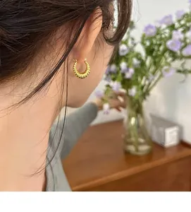 Detail view of model wearing gold-tone twisted croissant hoop earrings with elegant texture