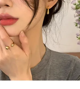 Detail of gold geometric horn earrings and double bead ring on model with indoor decor