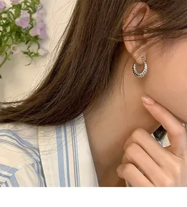 Close-up of silver croissant textured hoop earrings worn on ear with metallic finish