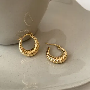 Close-up of golden croissant style twisted hoop earrings on minimalist ceramic surface