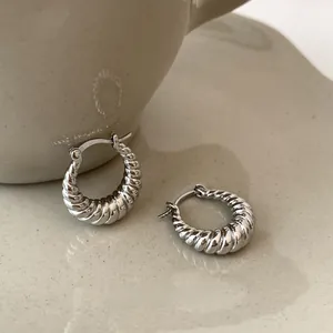 Detail shot of silver croissant hoop earrings with ribbed texture on a ceramic tray