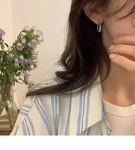 Detail of twisted silver hoop earrings worn with a casual striped shirt and lavender background