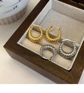Detailed view of gold and silver twisted horn hoop earrings in a wooden jewelry box