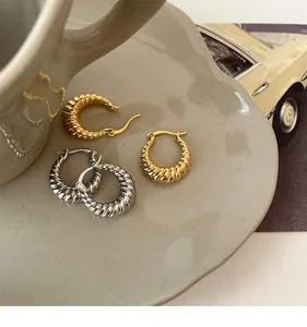 Detail of twisted croissant hoop earrings in gold and silver finish on ceramic tray