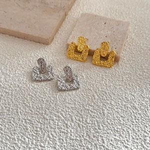 Macro shot of geometric square earrings with hammered texture in gold and silver plating