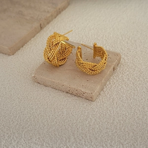 Golden woven texture hoop earrings with twisted knot design on neutral stone background