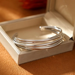 Polished silver multi-layer open cuff bracelet displayed in a beige jewelry gift box