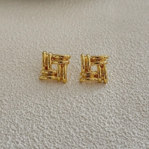 Close-up of geometric square woven earrings with a polished gold finish and textured design