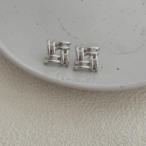 Elegant silver square stud earrings featuring a textured woven metal design on white ceramic