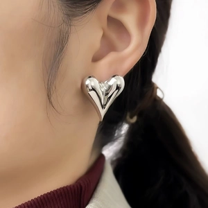 Minimalist silver heart stud earrings with high-polish metallic finish on female model